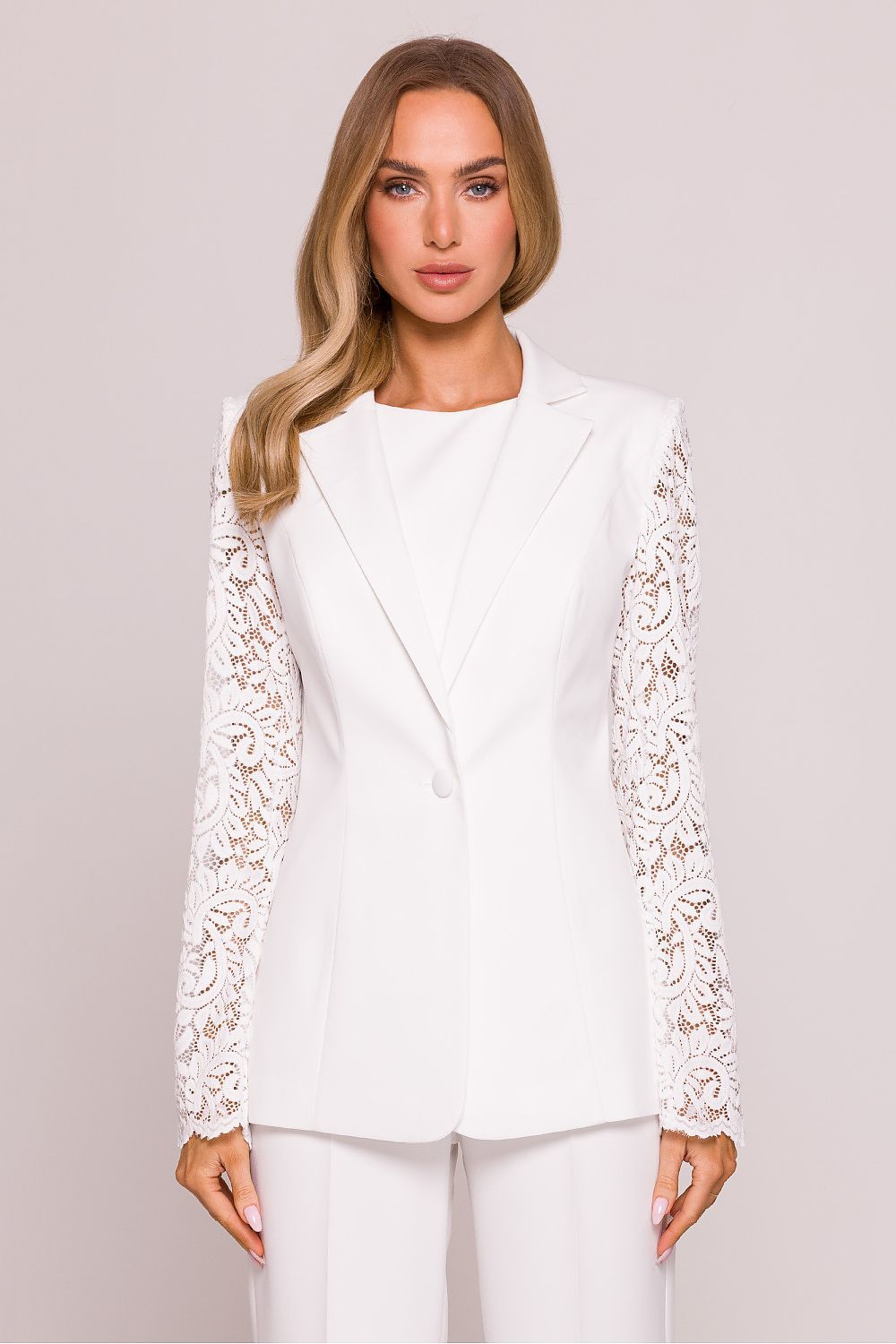 Woman wearing a white blazer with lace sleeves on a plain background