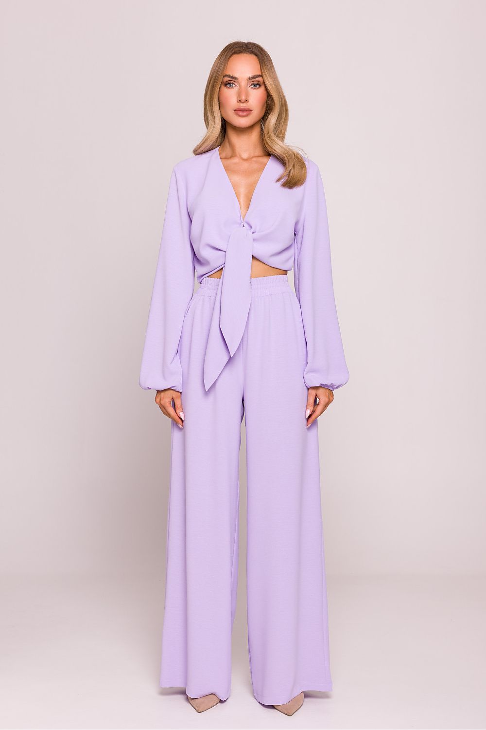 Woman wearing a lavender outfit with a matching jacket and wide-leg pants on a plain background