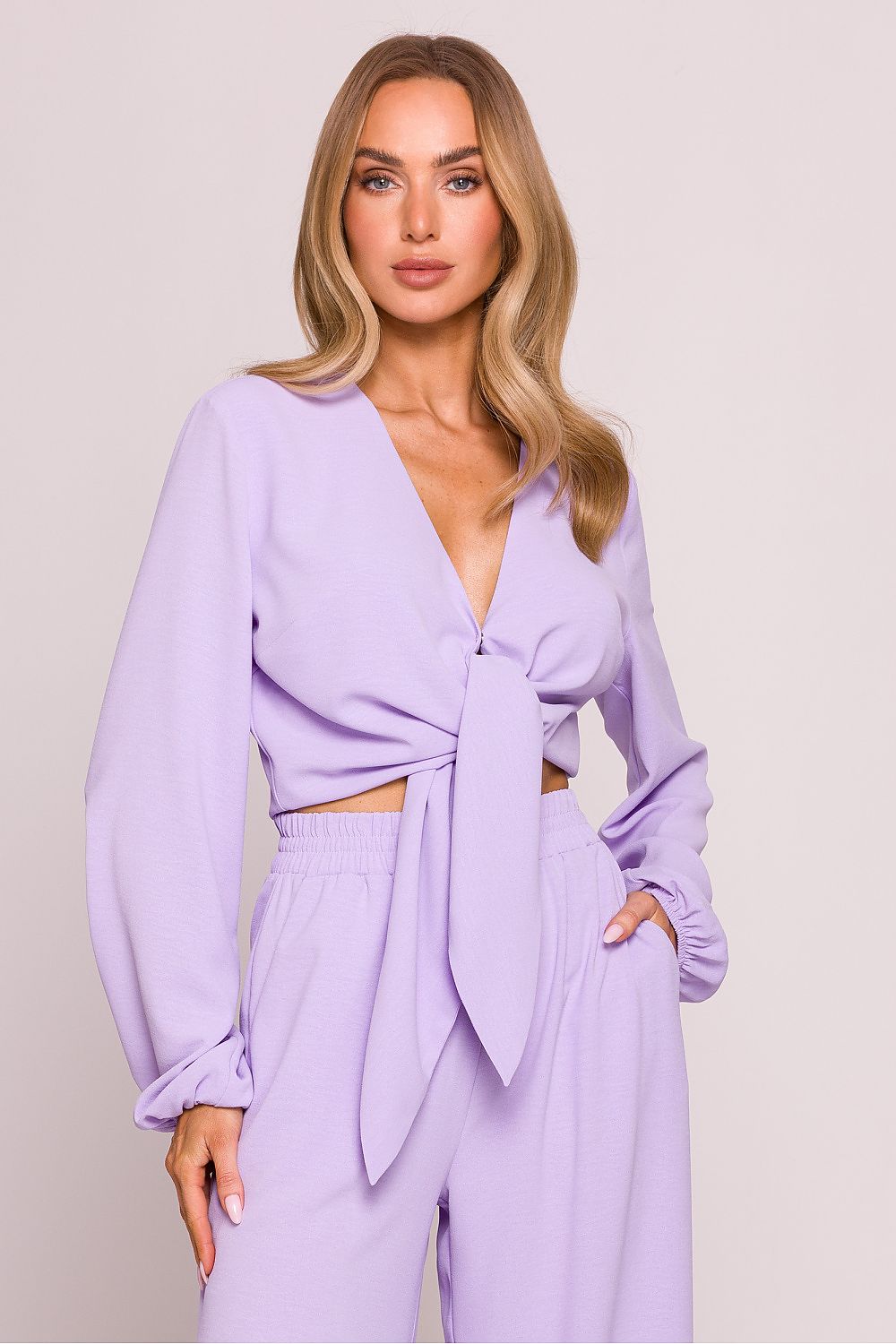 Woman wearing a lavender outfit with a matching top and pants on a plain background