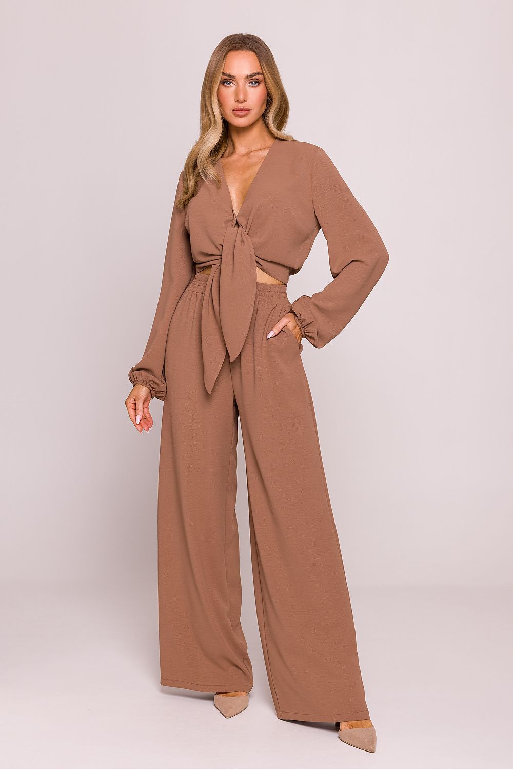 Woman wearing a brown jumpsuit on a light pink background