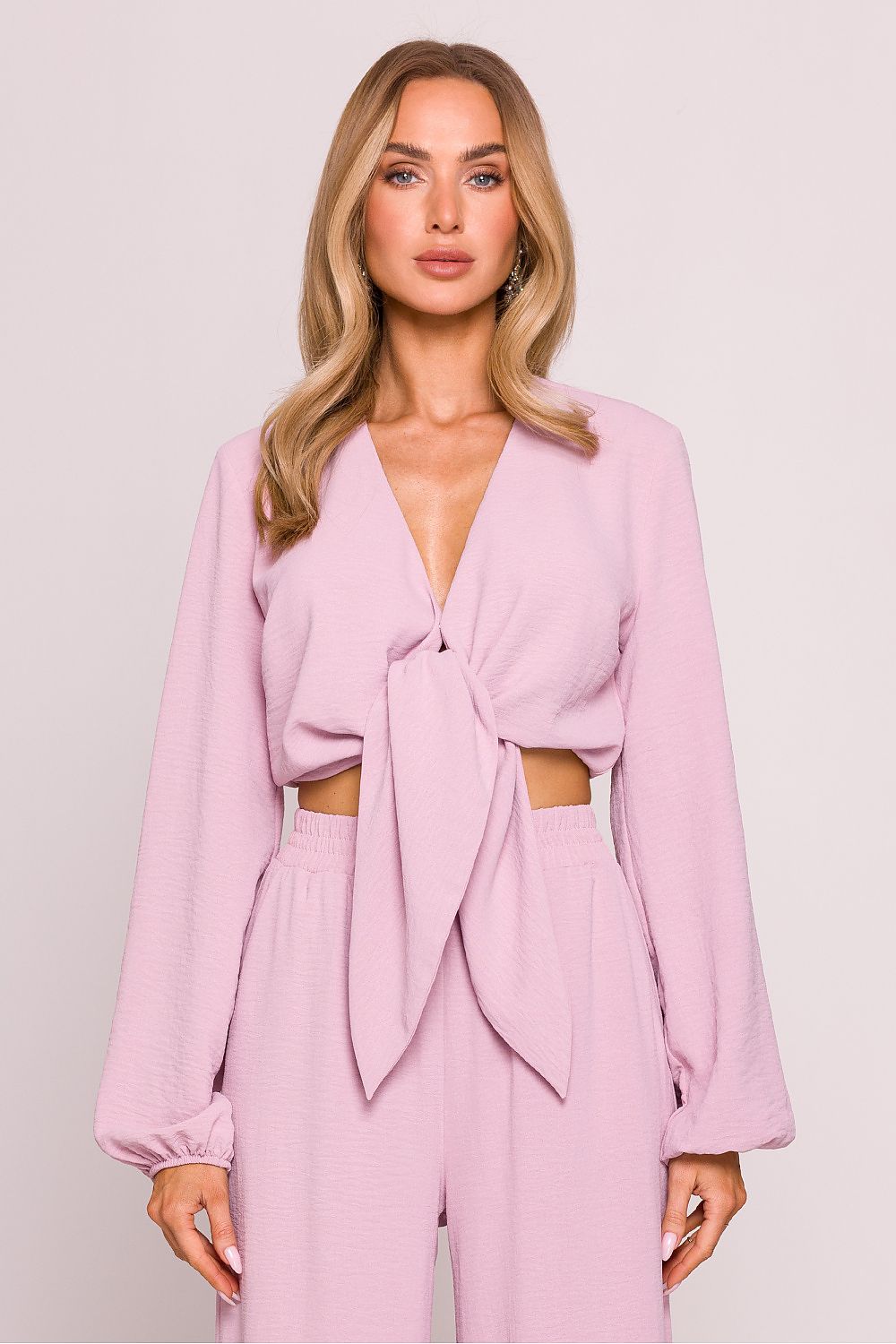 Woman wearing a pink outfit with a tied top against a plain background