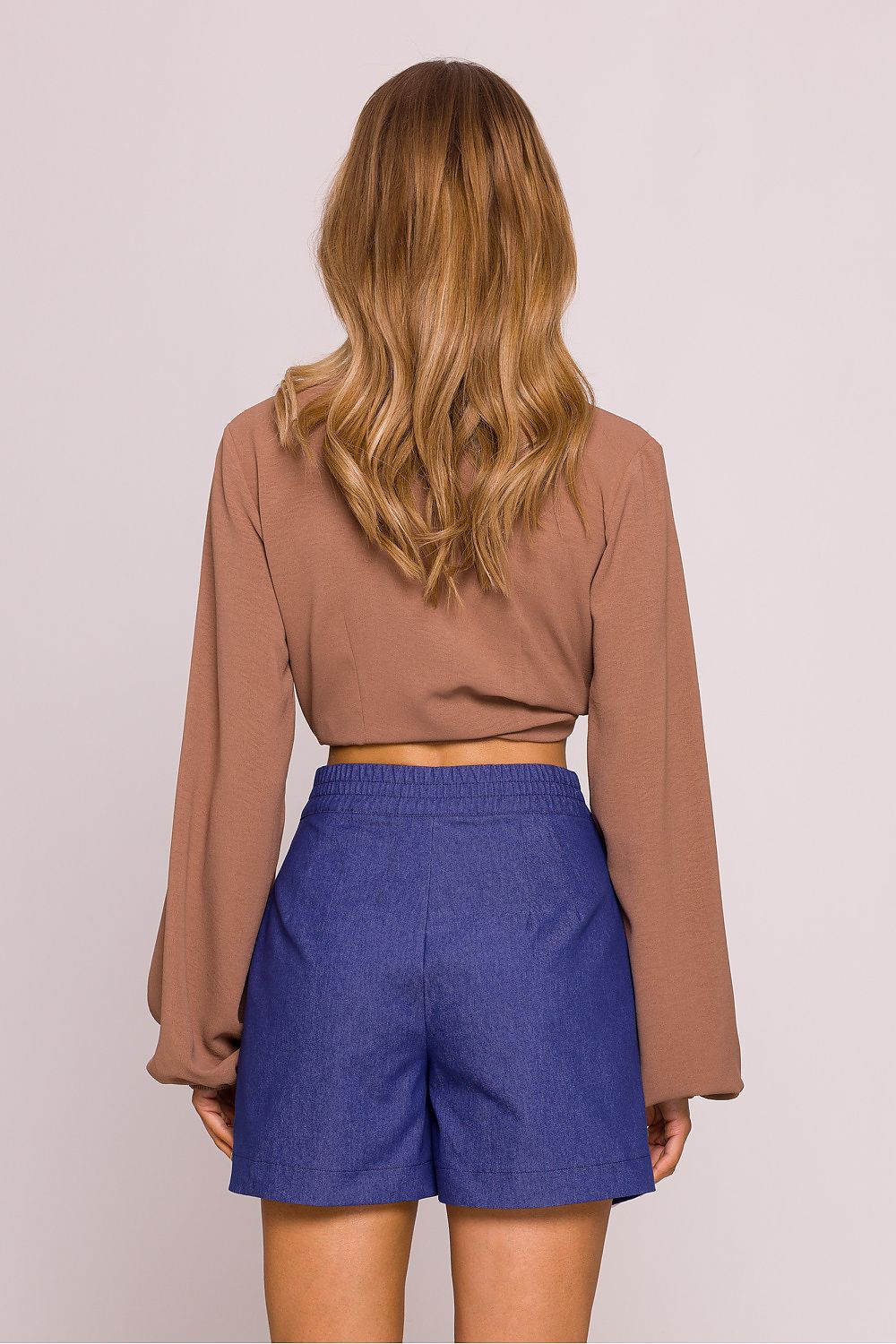 Person wearing a brown long-sleeve top and blue shorts on a plain background