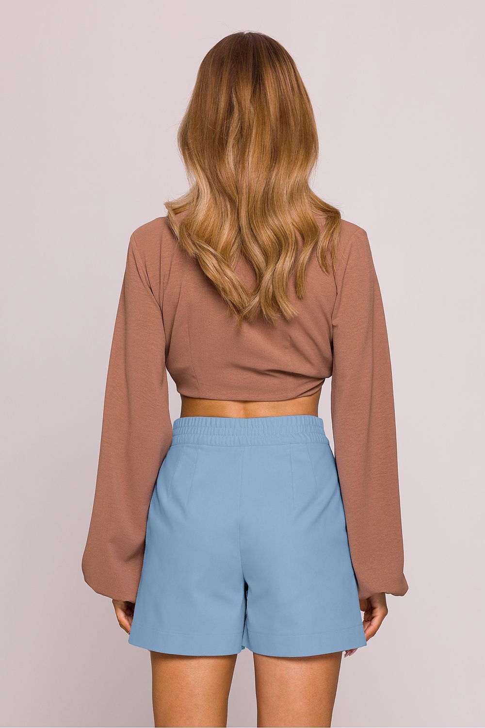 Person wearing a brown long-sleeve top and light blue shorts on a plain background