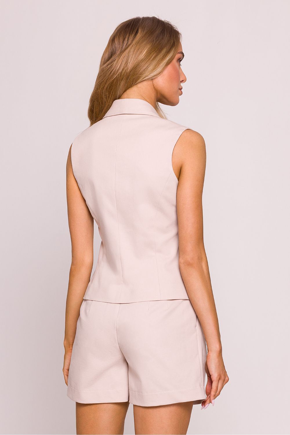 Woman wearing a beige sleeveless top and shorts set on a plain background