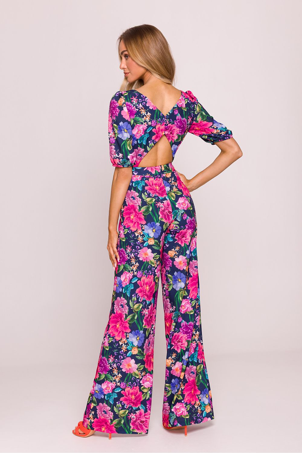 Woman wearing a colorful floral jumpsuit on a plain background