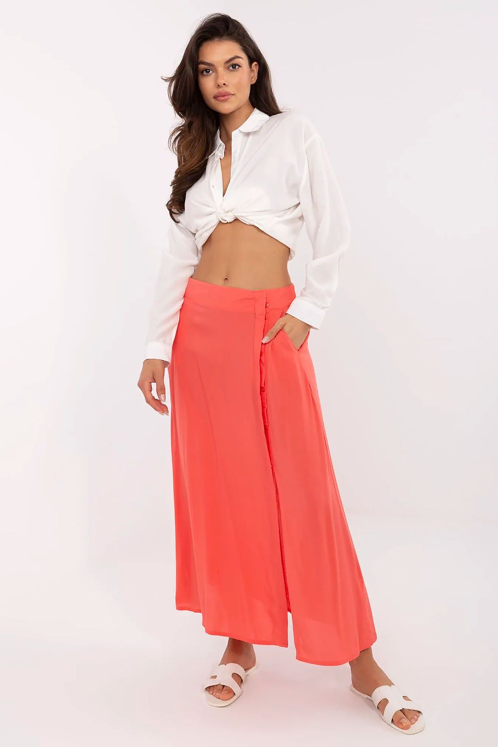 Woman wearing a white blouse and coral wide-leg pants on a white background