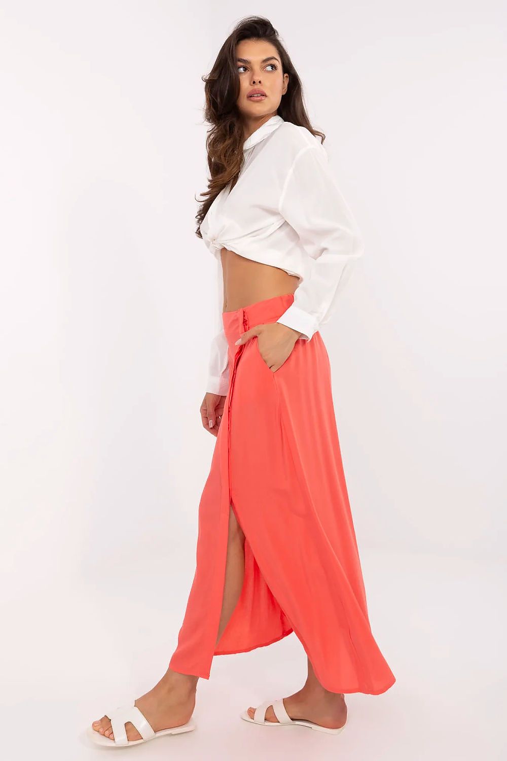 Woman wearing a white cropped top and coral maxi skirt on a white background