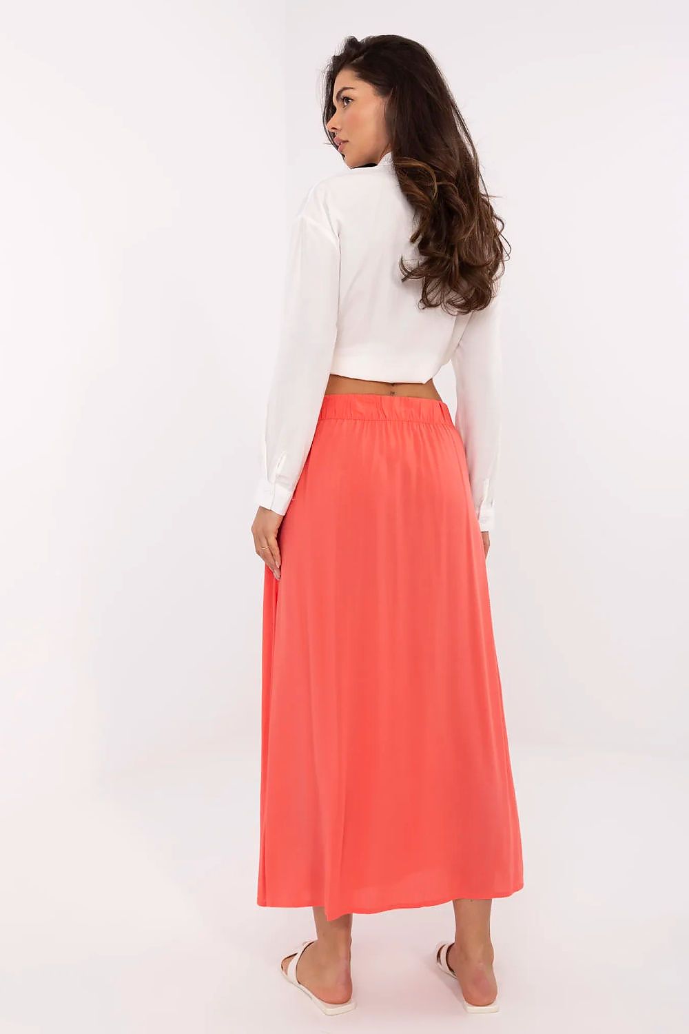 Woman wearing a white top and coral skirt on a white background