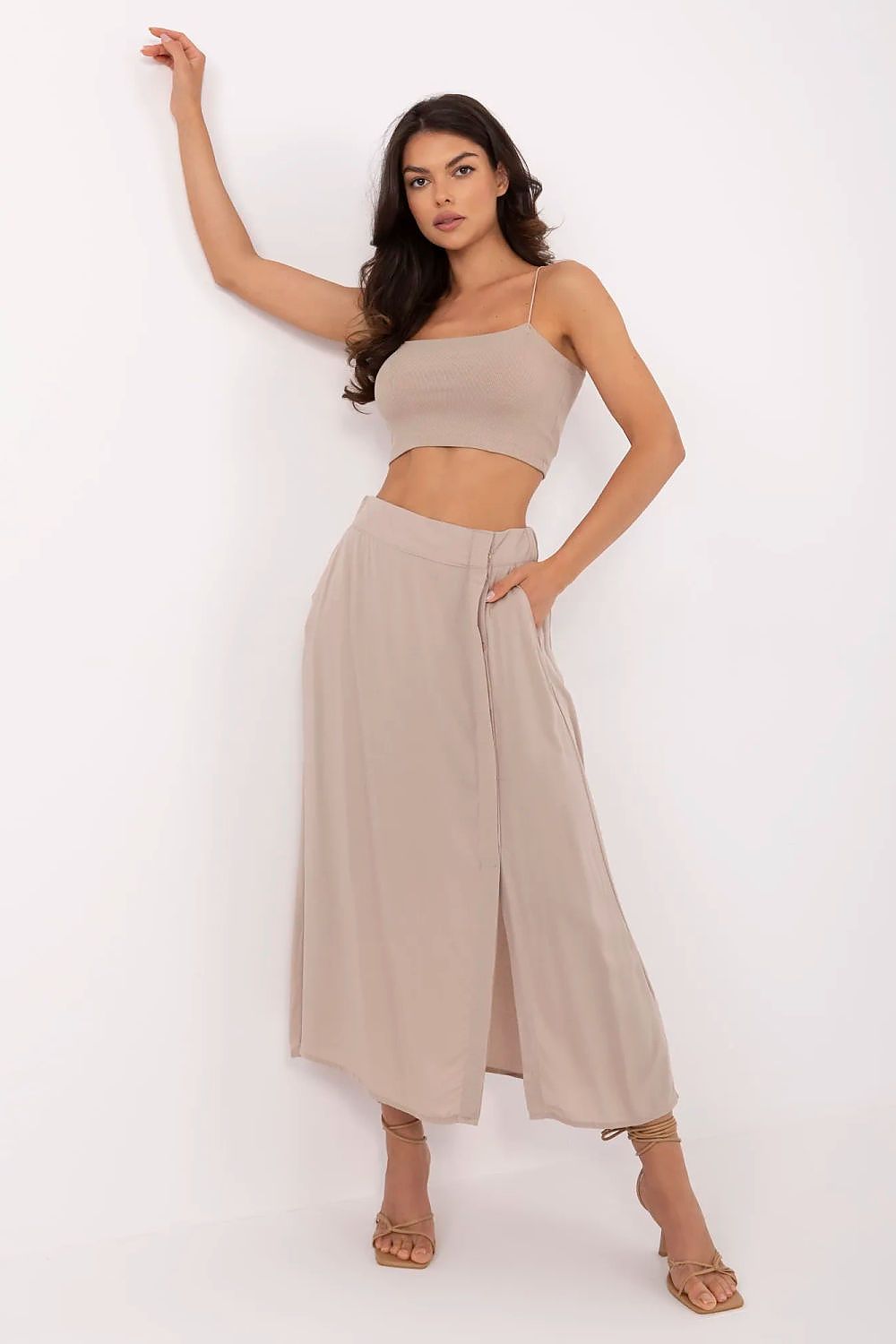 Woman wearing a beige top and wide-leg pants against a white background