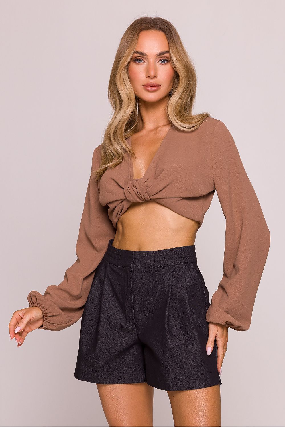 Woman wearing a brown long-sleeve top and black shorts on a plain background