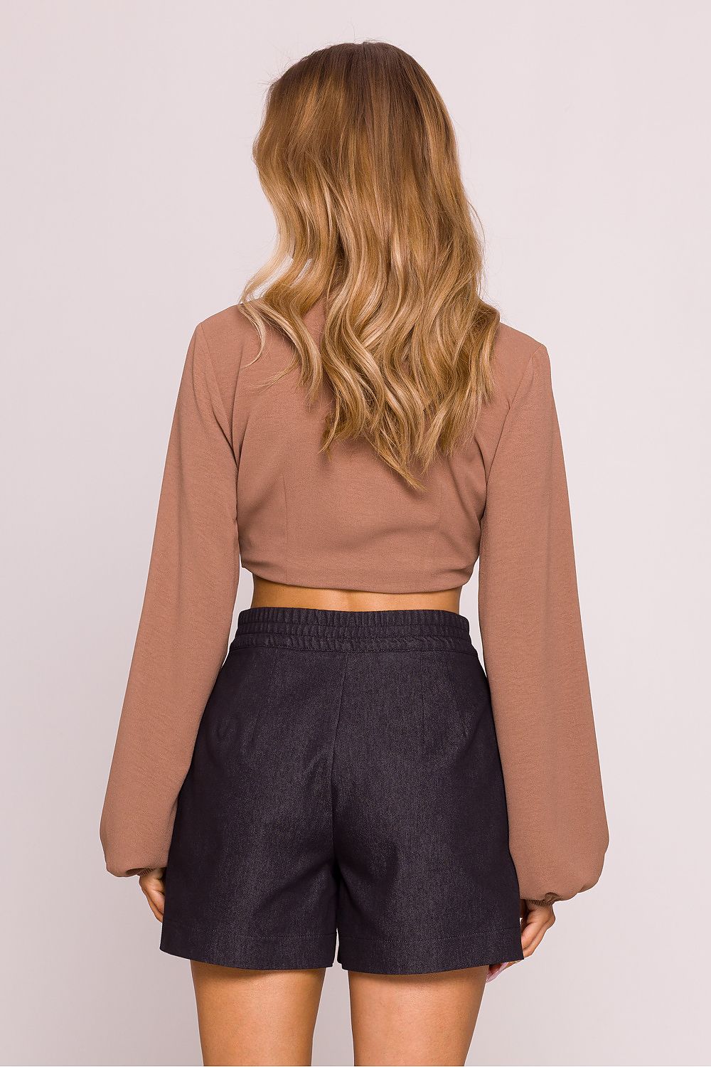 Person wearing a brown long-sleeve top and black shorts on a light pink background