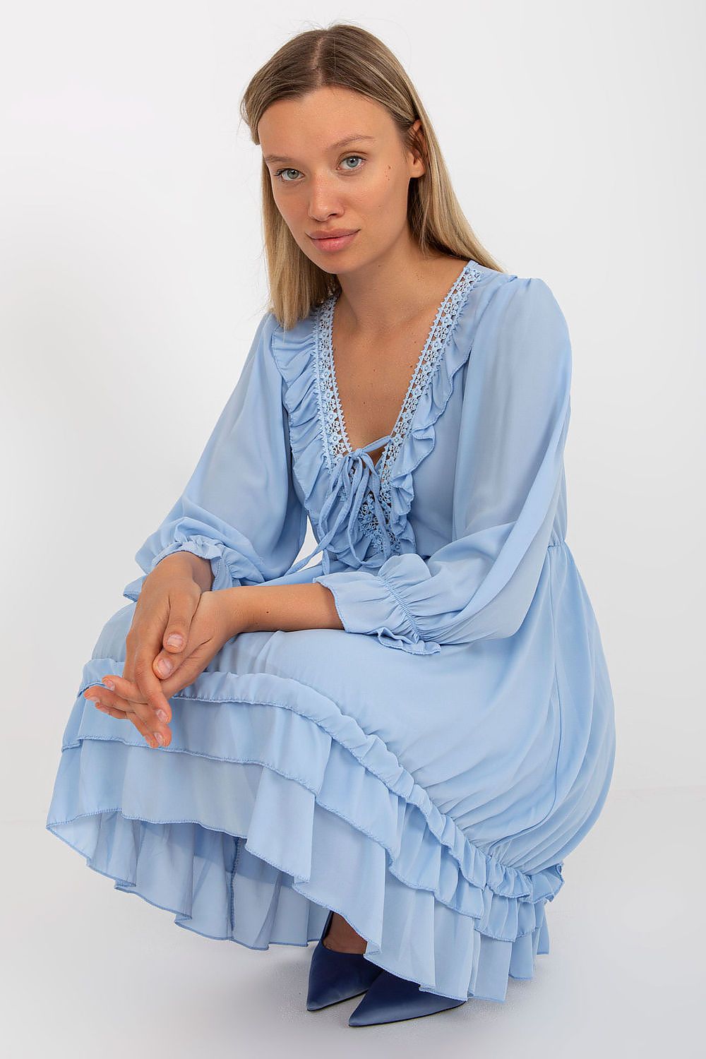 Woman wearing a light blue dress with ruffled sleeves and hem on a white background