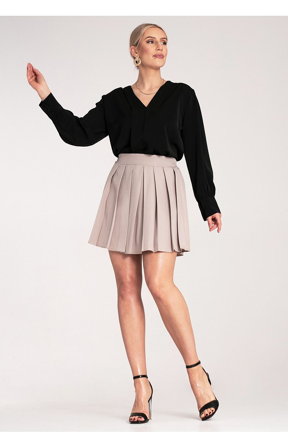 Woman wearing a black top and beige pleated skirt on a white background