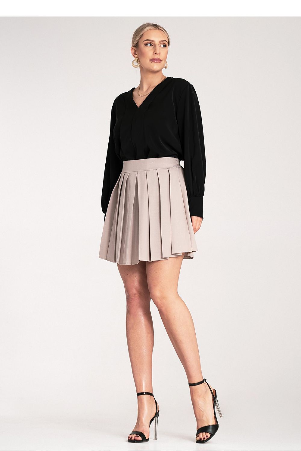 Woman wearing a black top and beige pleated skirt on a white background