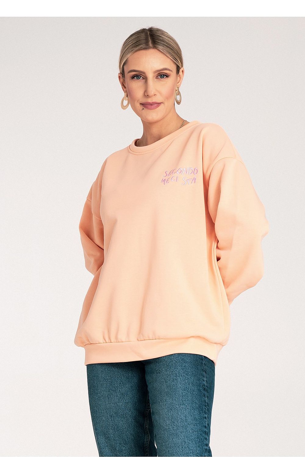 Woman wearing a peach oversized sweatshirt with text on a plain background