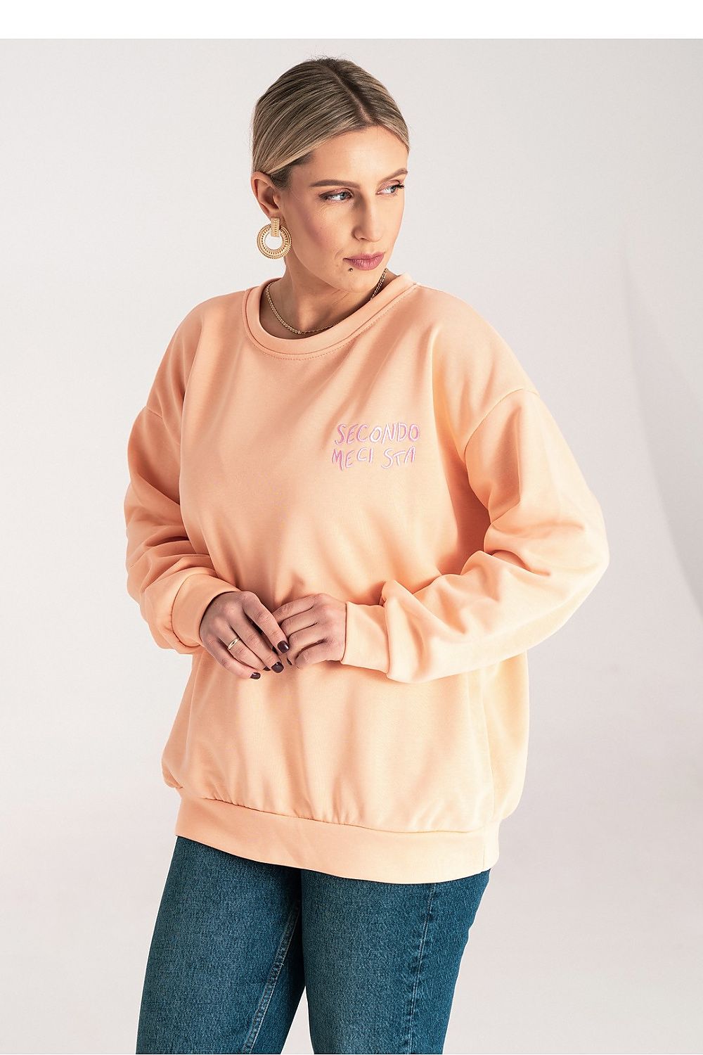 Woman wearing a peach-colored sweatshirt with text on a plain background