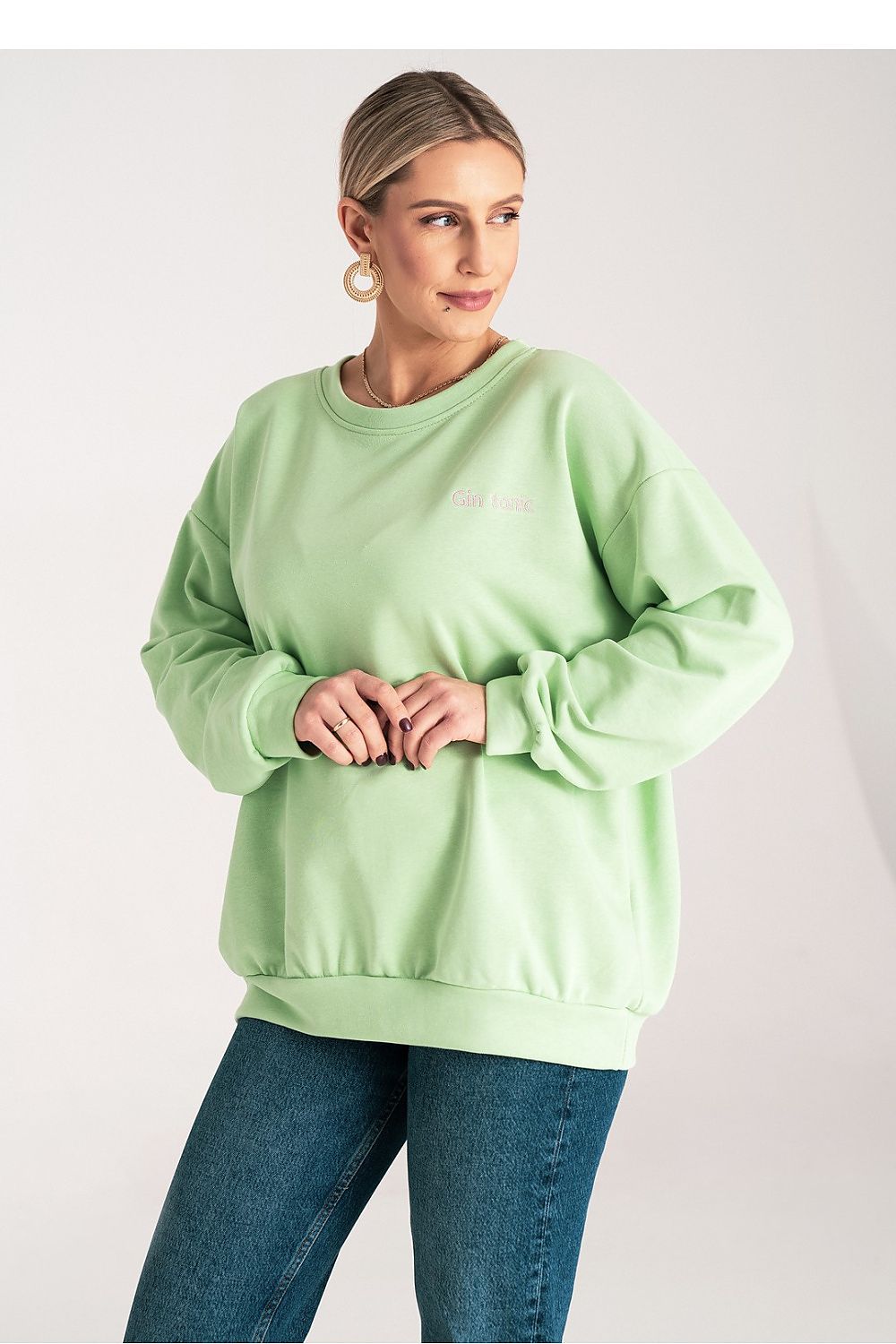 Woman wearing a light green sweatshirt and blue jeans on a white background
