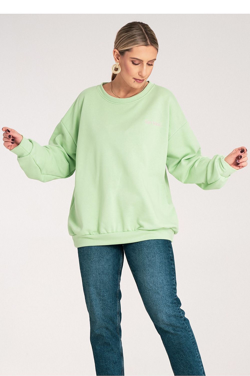 Woman wearing a light green sweatshirt and blue jeans on a white background