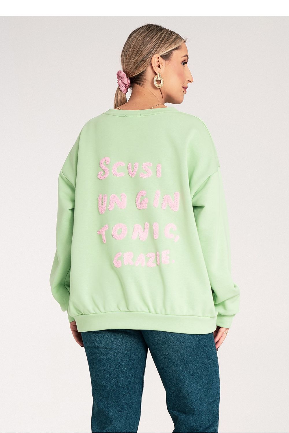 Person wearing a light green sweatshirt with pink text on a plain background