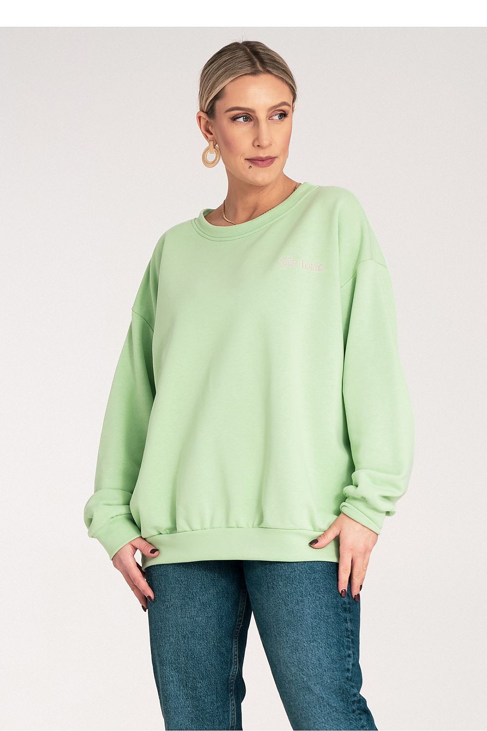 Woman wearing a light green sweatshirt and blue jeans on a white background