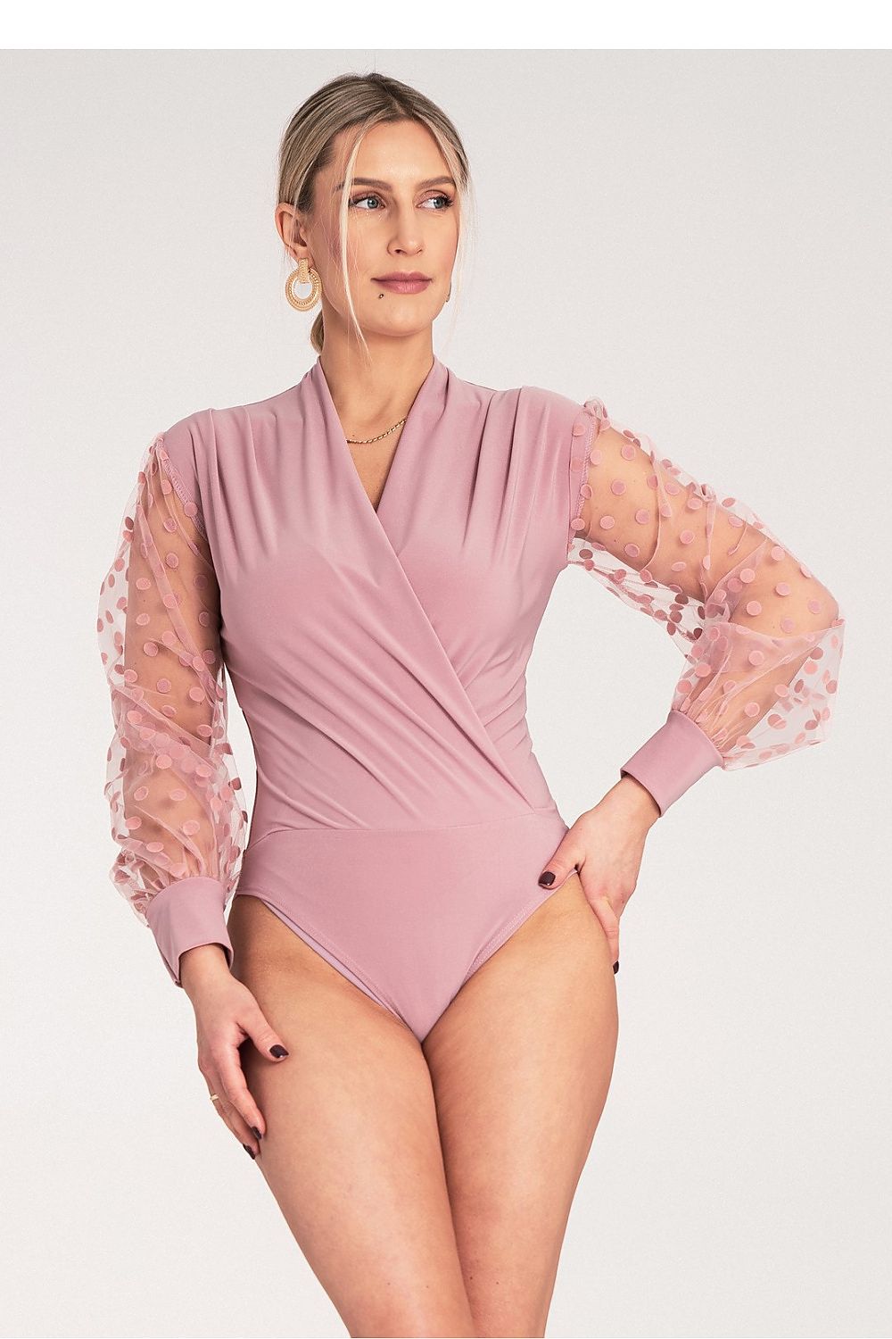 Woman wearing a pink swimsuit with sheer sleeves on a white background