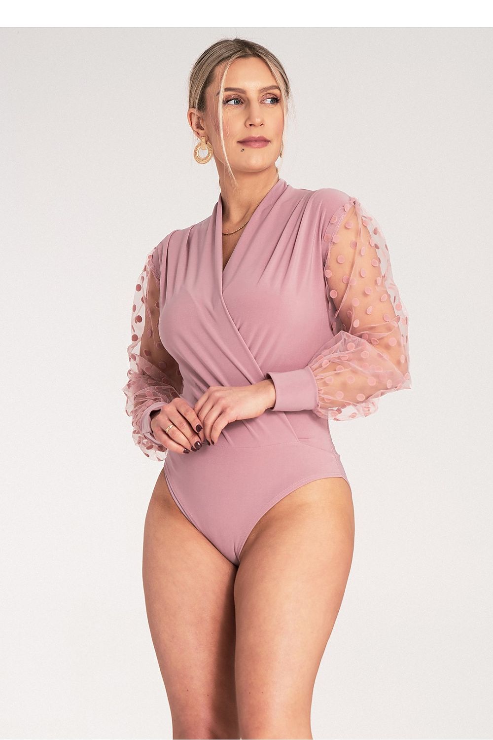 Woman wearing a pink swimsuit with sheer sleeves on a white background