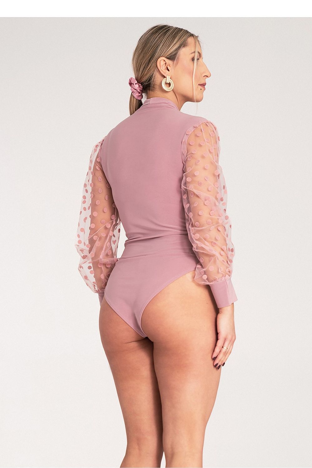 Woman wearing a pink bodysuit with sheer sleeves on a white background
