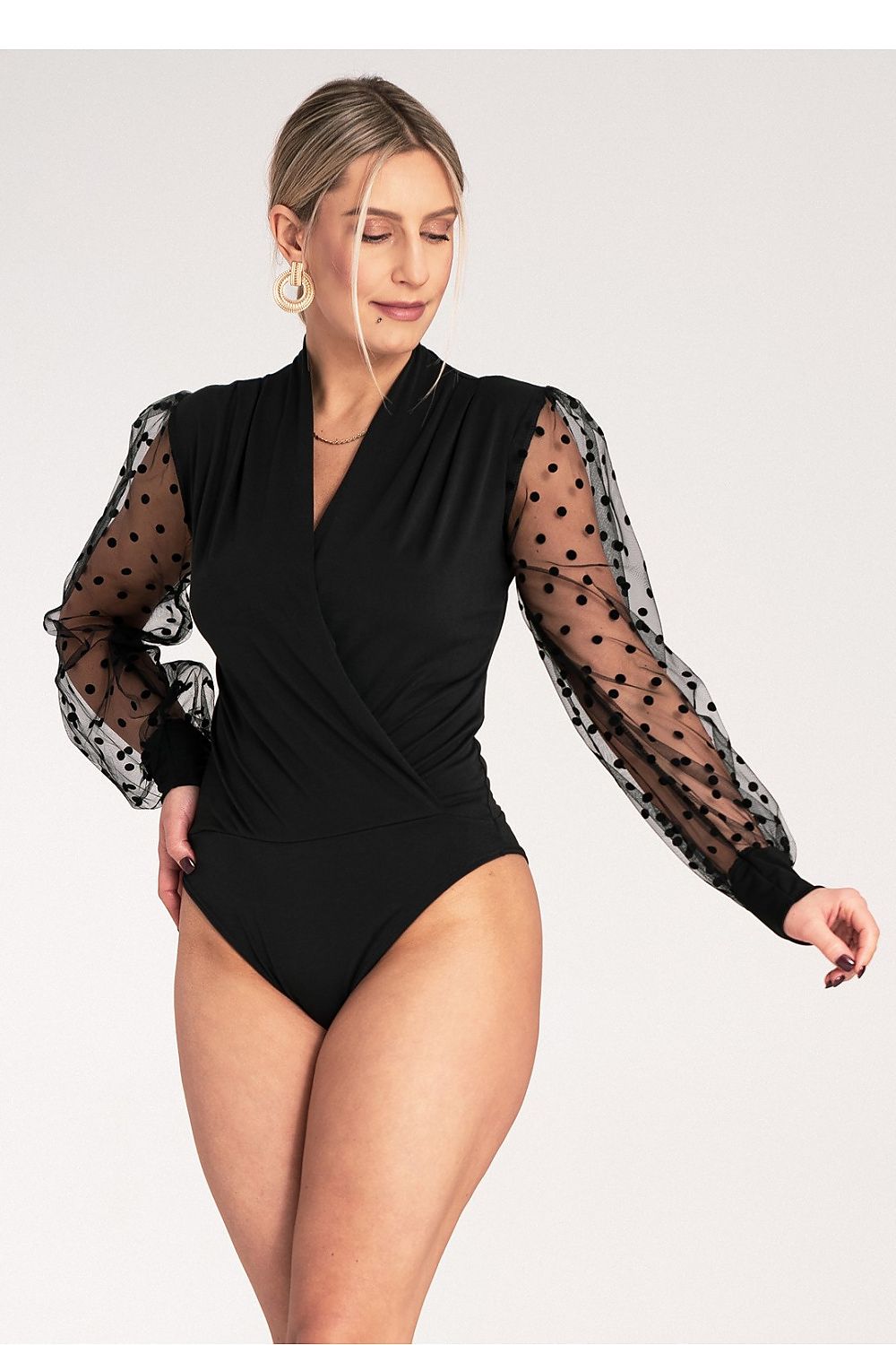Woman wearing a black bodysuit with sheer sleeves on a white background