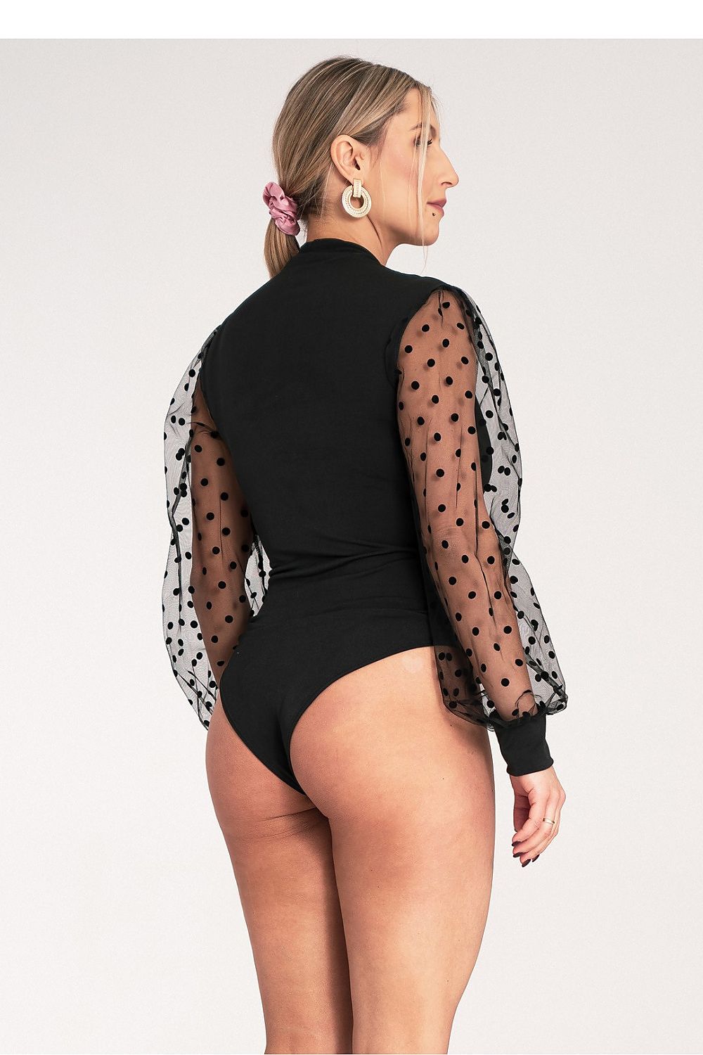 Woman wearing a black bodysuit with sheer sleeves on a white background