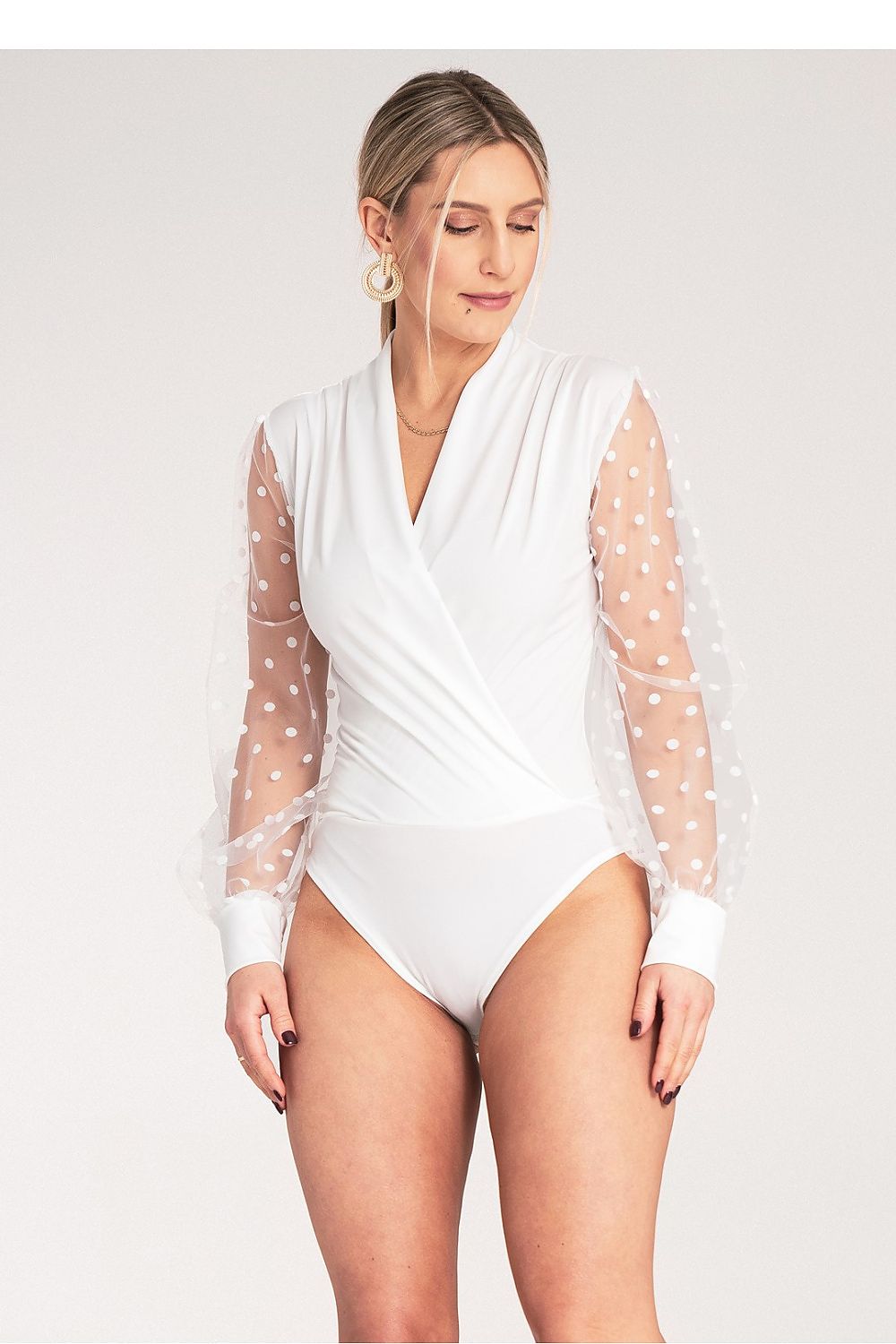 Woman wearing a white bodysuit with sheer sleeves on a plain background