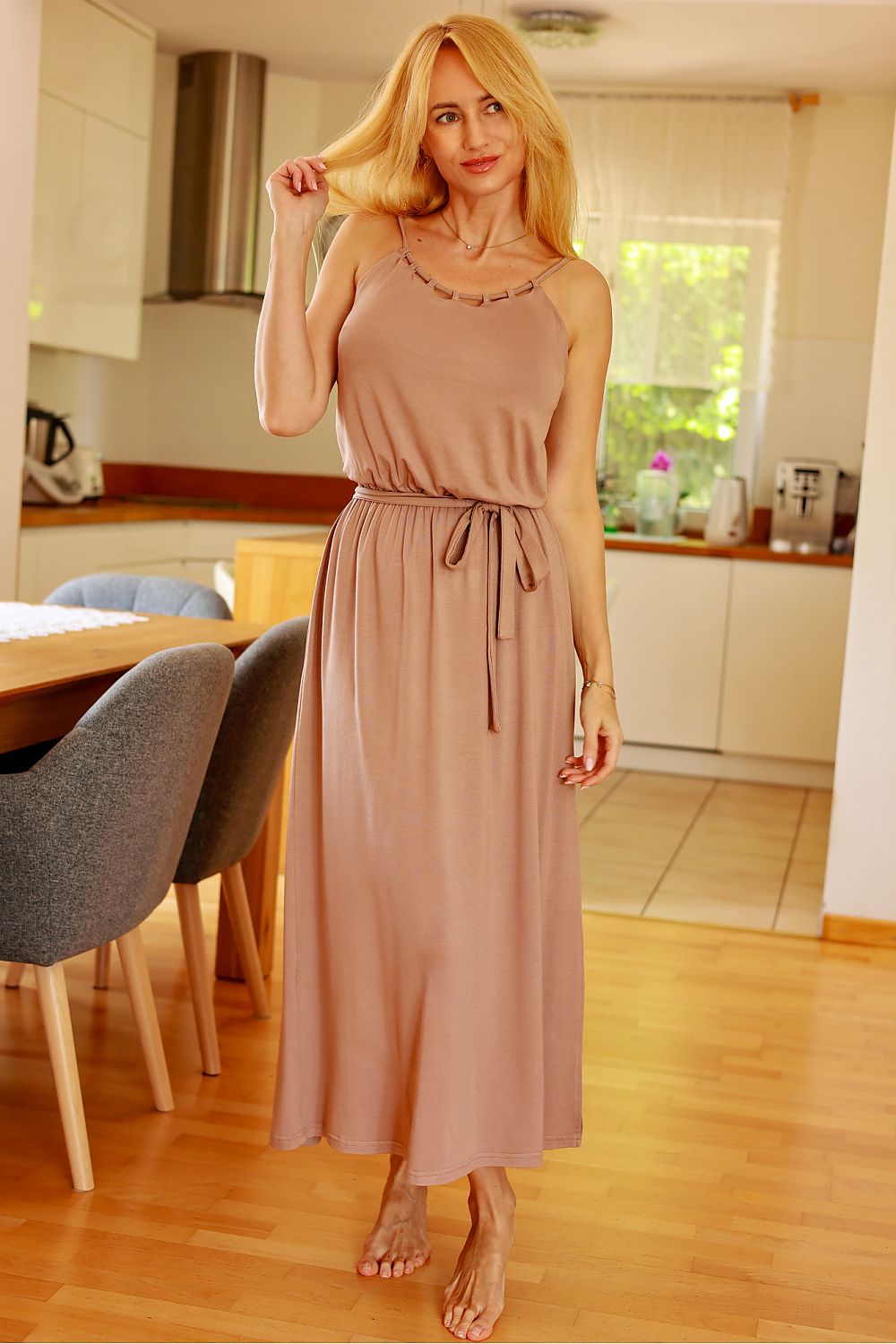 Woman in a long pink dress standing in a kitchen.