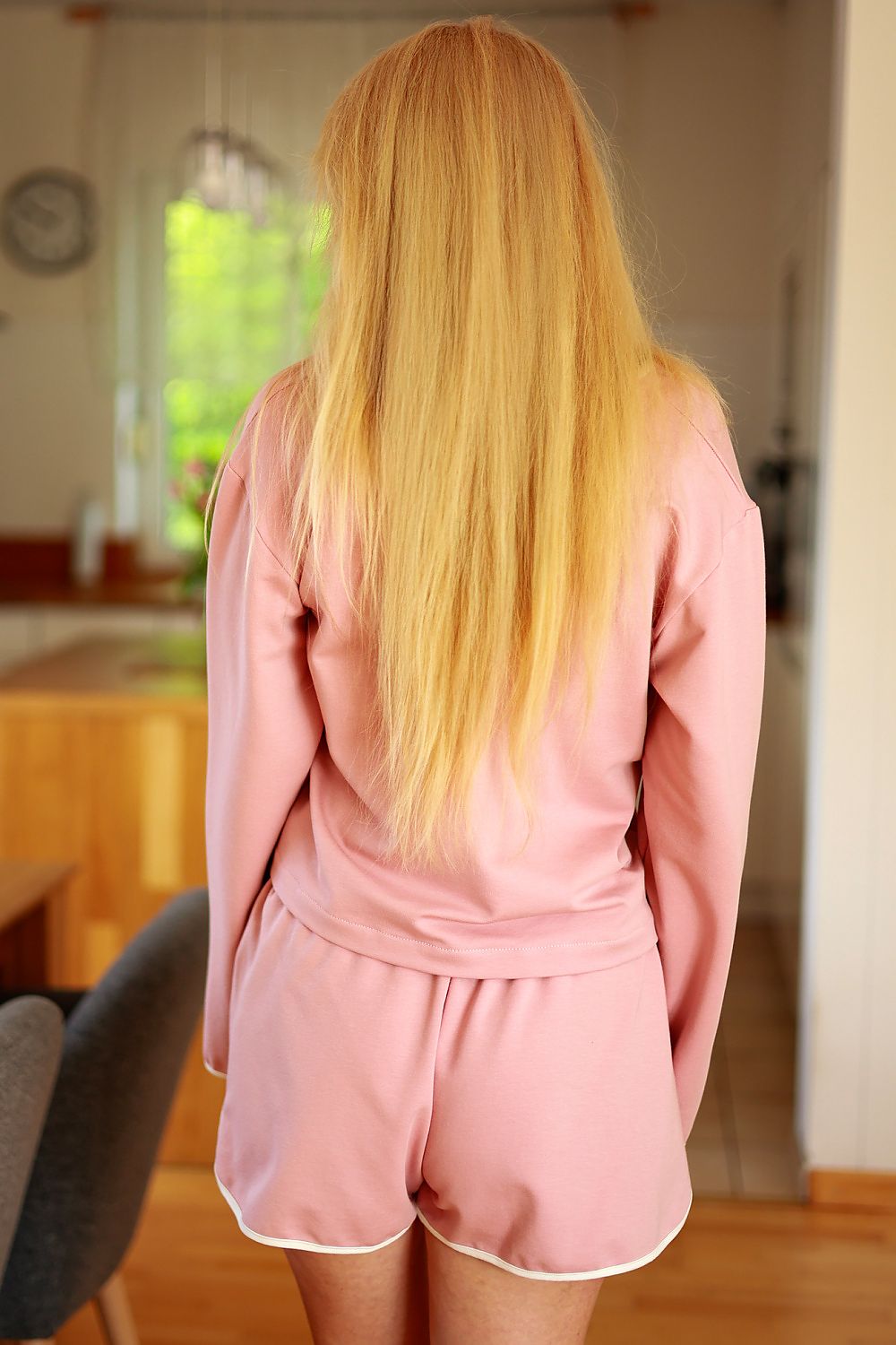 Person wearing a pink robe in a room with a window and furniture.