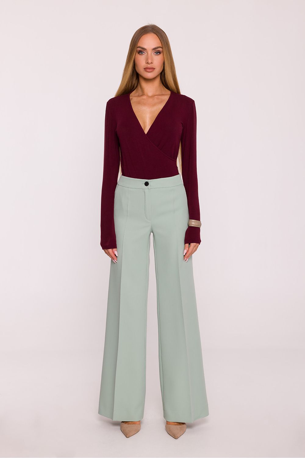 Woman wearing a burgundy top and light green pants on a white background