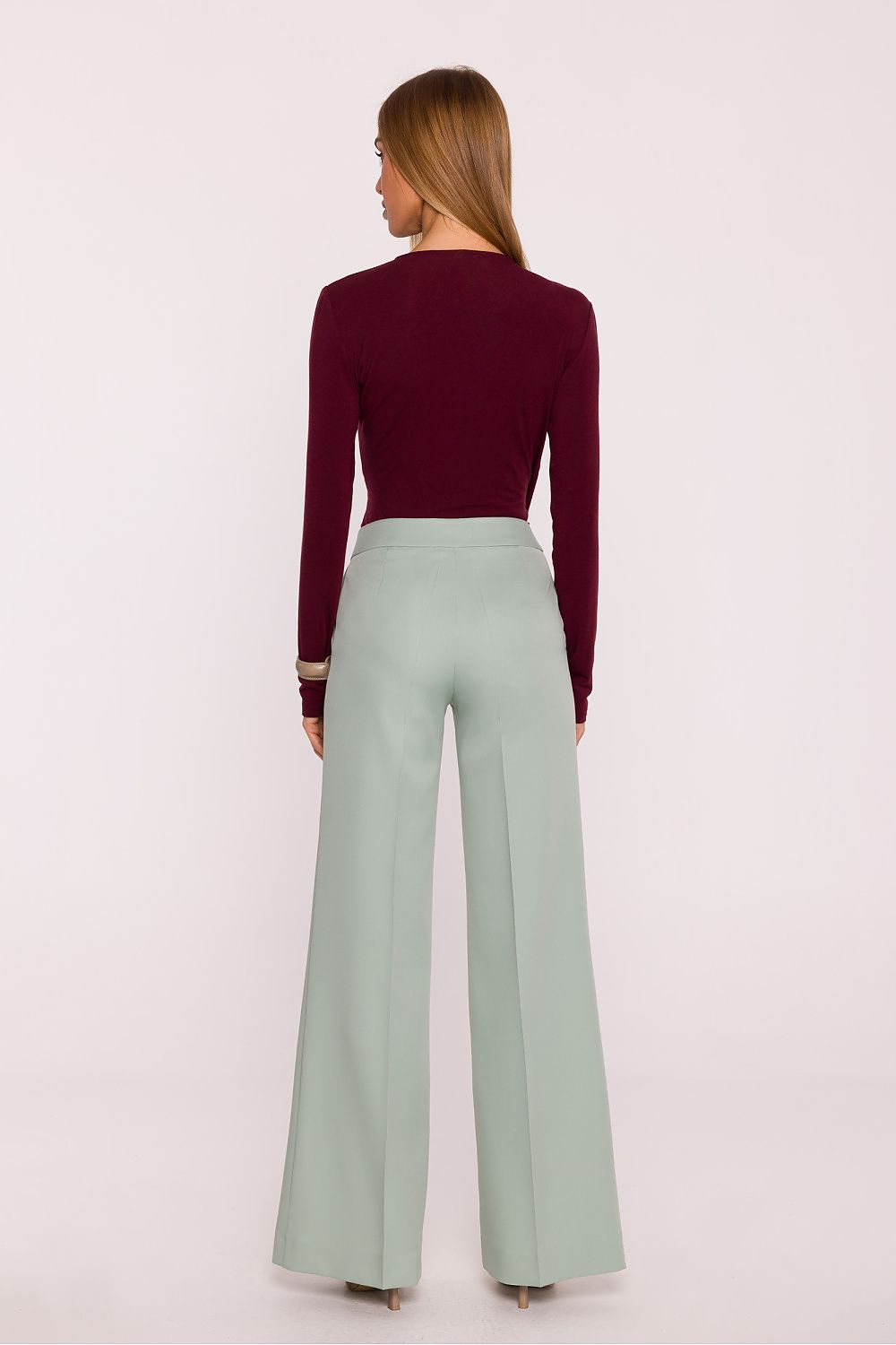 Woman wearing a burgundy sweater and light green wide-leg pants on a white background