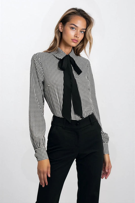 Woman wearing a black and white checkered blouse with a black tie and black pants on a white background
