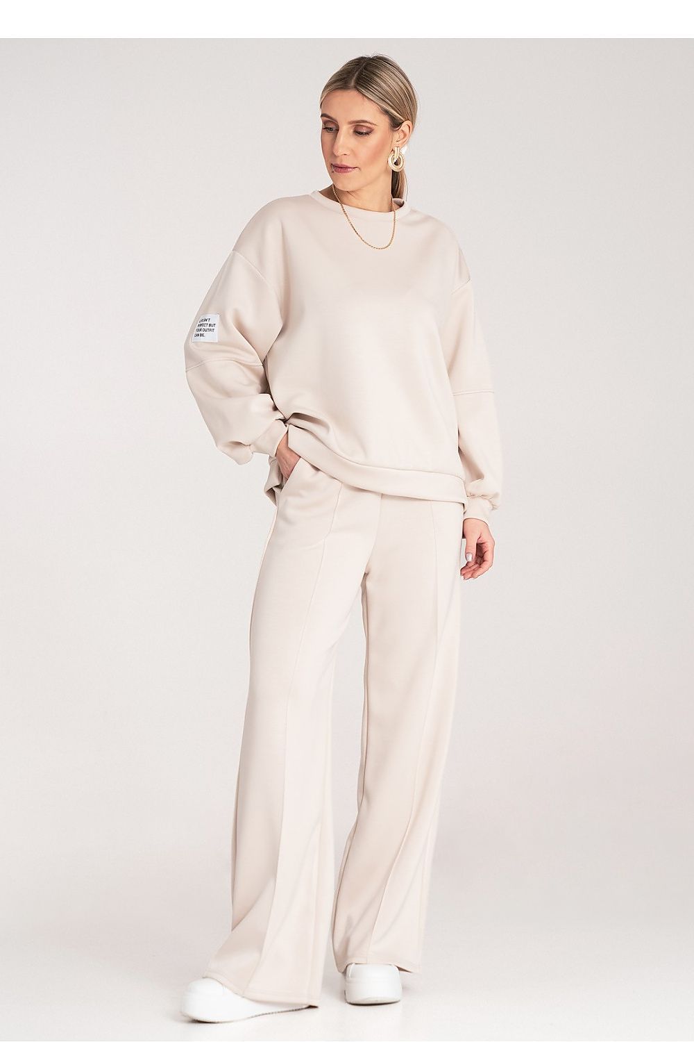 Woman wearing a beige sweatshirt and pants set on a white background