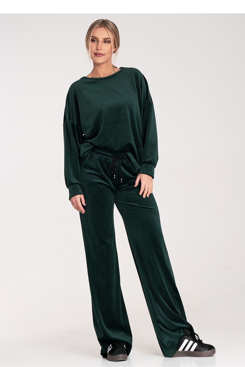 Person wearing a green tracksuit with Adidas shoes on a white background