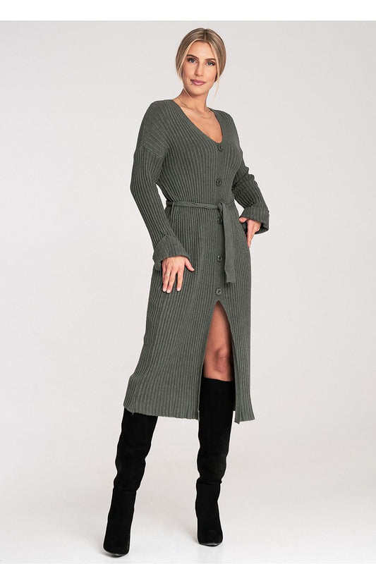 Woman wearing a long green ribbed dress with a belt and black knee-high boots on a white background