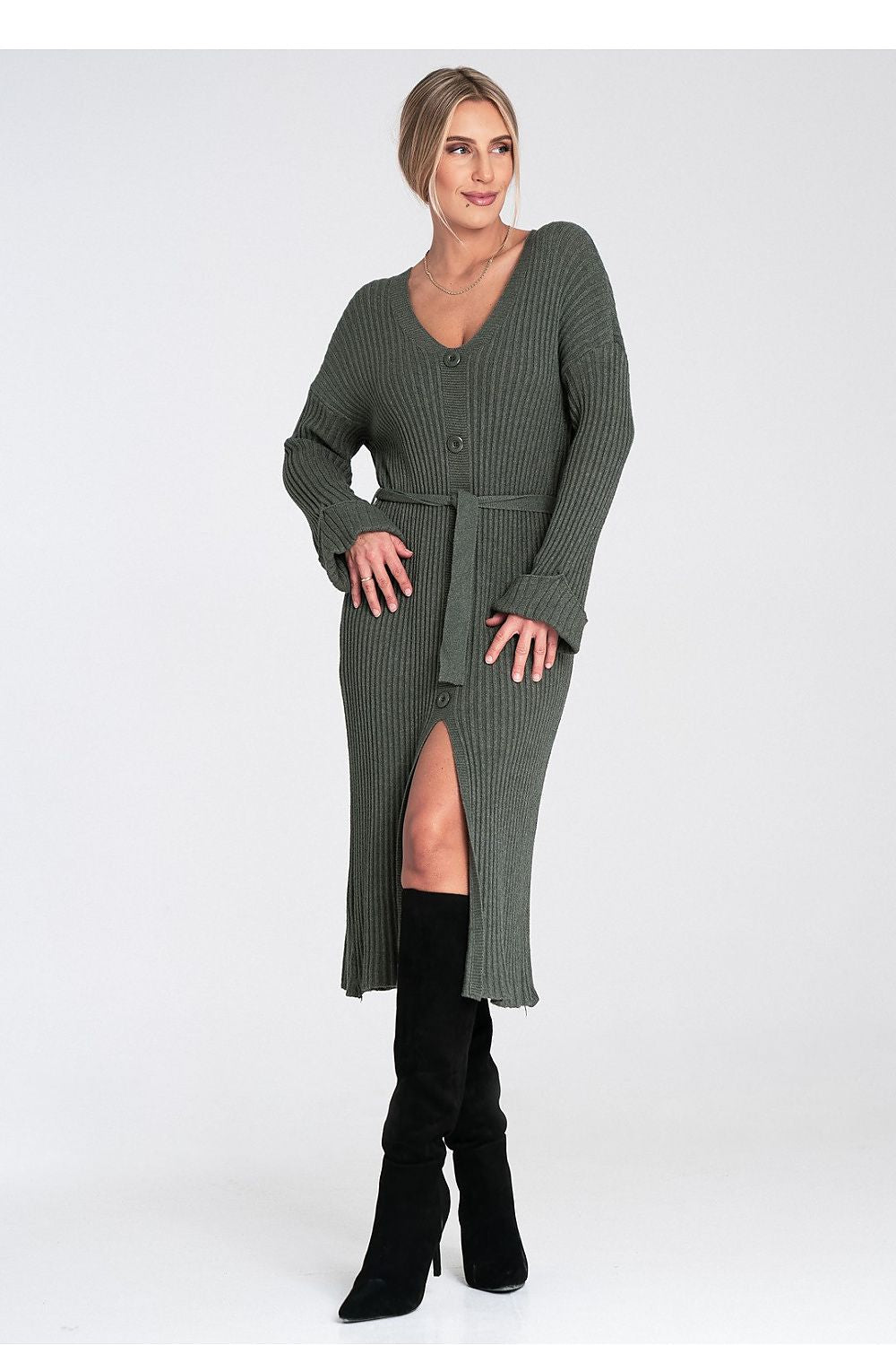 Woman wearing a long green ribbed dress with a belt on a white background