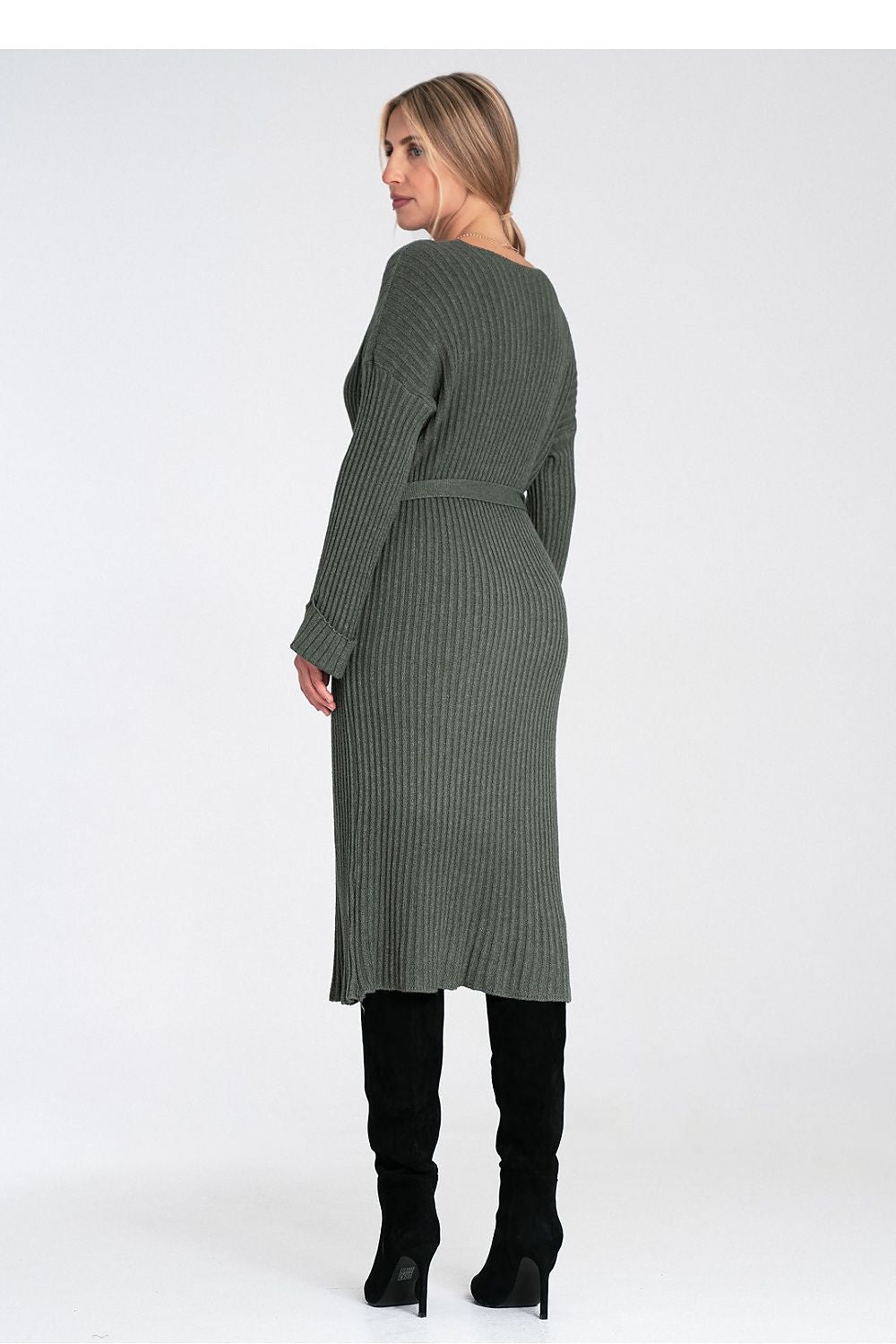 Woman wearing a green ribbed dress with black boots on a white background