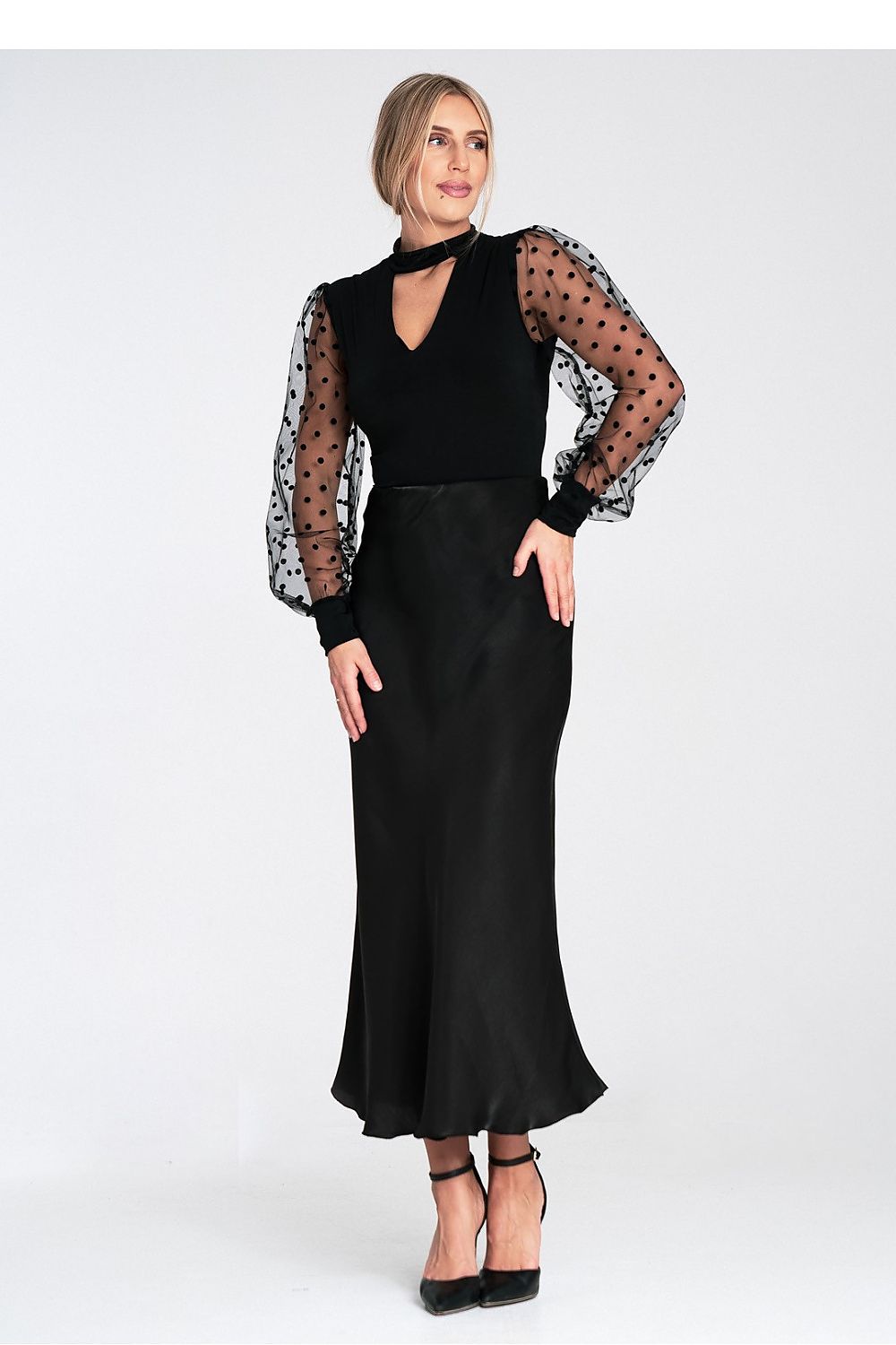 Woman wearing a black outfit with sheer sleeves on a white background