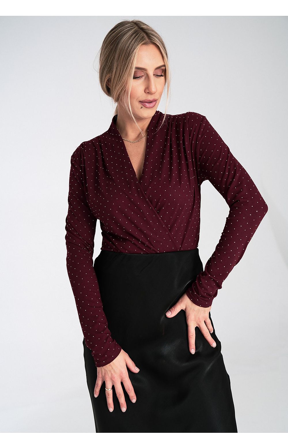Woman wearing a burgundy polka dot blouse and black skirt on a white background