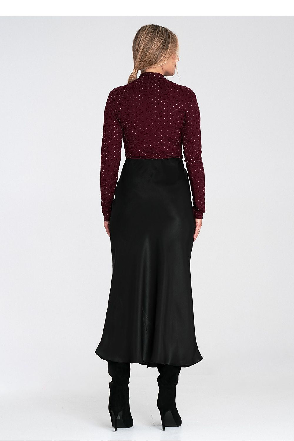Woman wearing a burgundy polka dot top and black satin skirt on a white background