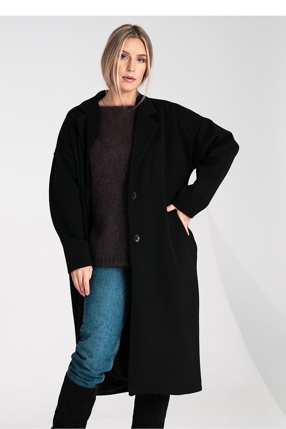 Woman wearing a black coat over a dark sweater and blue jeans on a white background