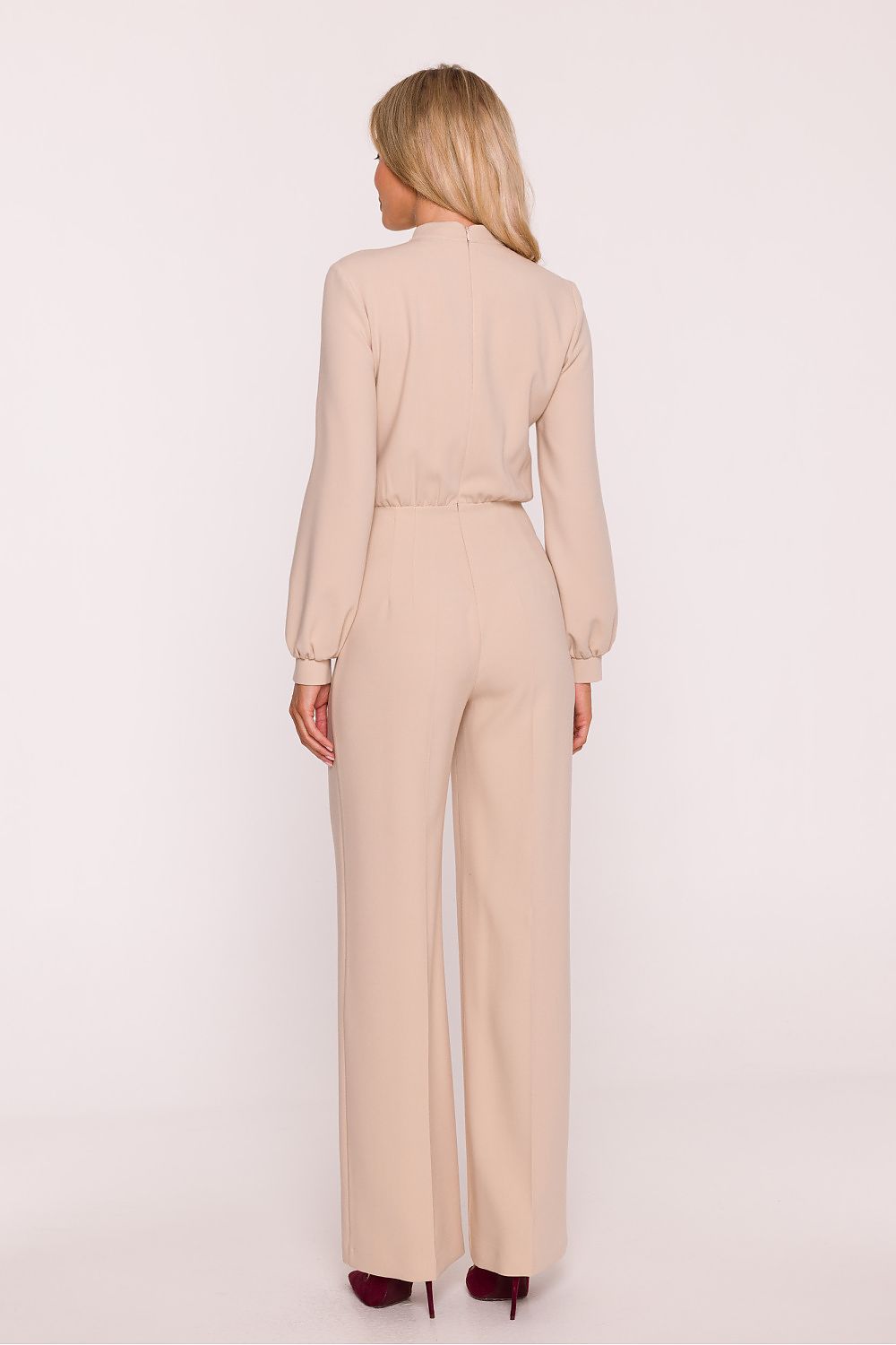Woman wearing a beige jumpsuit on a light pink background