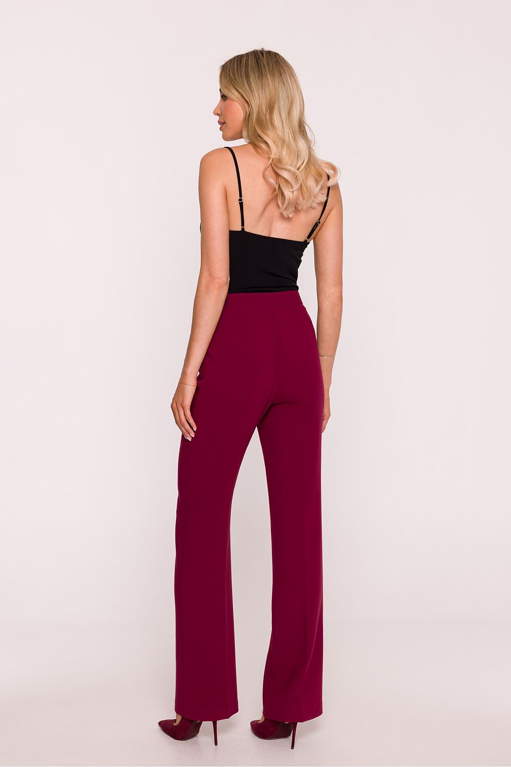 Woman wearing a black top and burgundy jumpsuit on a light pink background