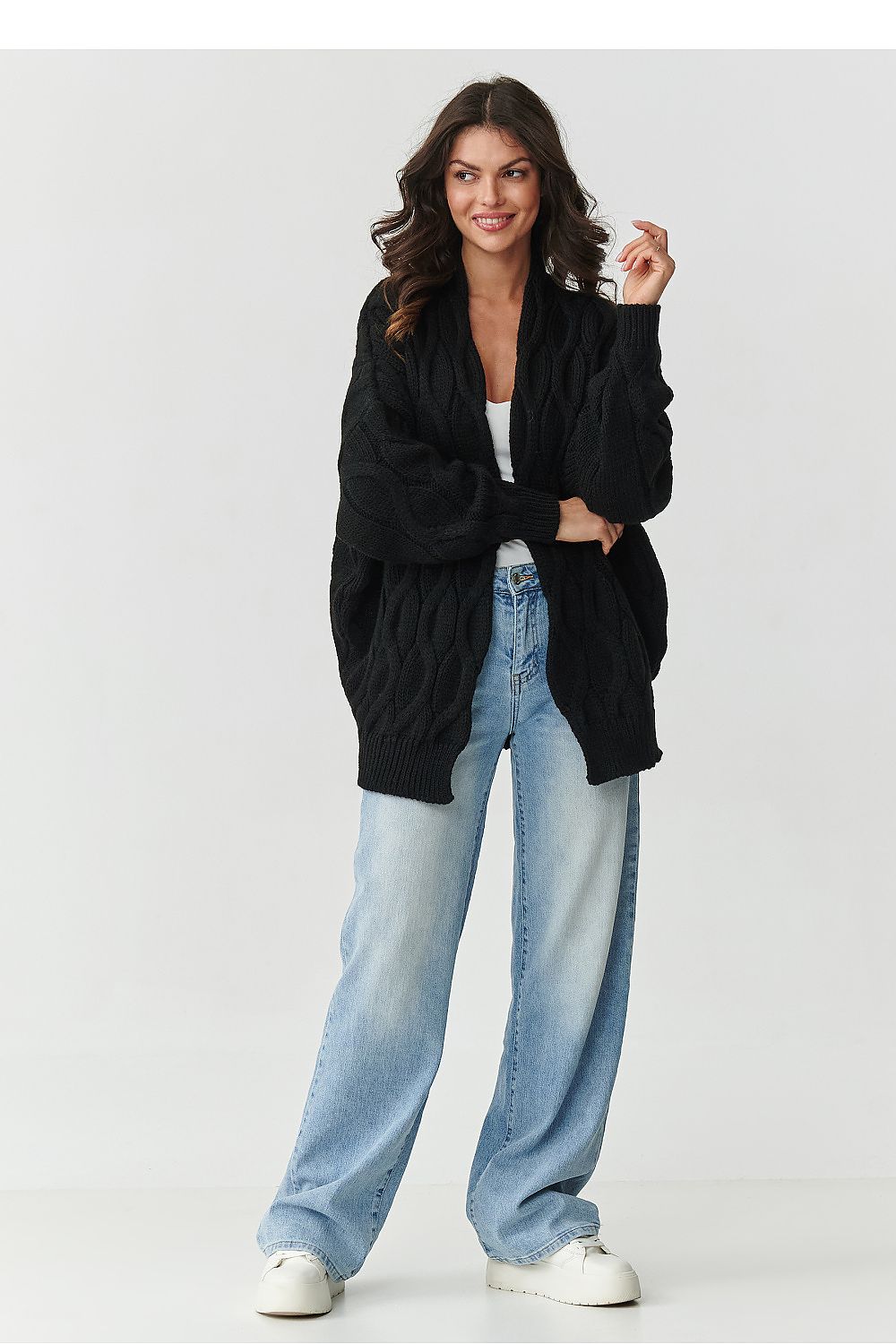 Woman wearing a black cardigan, white top, and light blue jeans on a white background