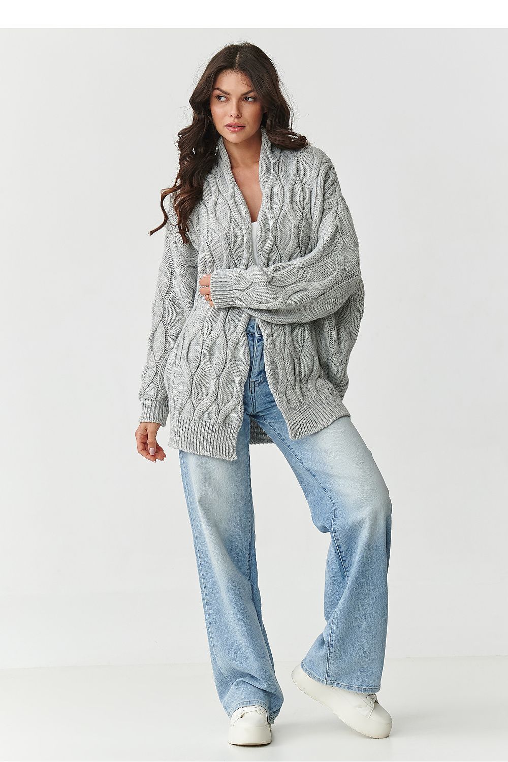 Woman wearing a gray cable knit sweater and light blue jeans on a white background