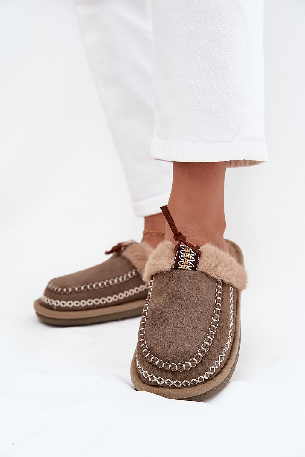 Brown slippers with fur trim worn by a person on a white background