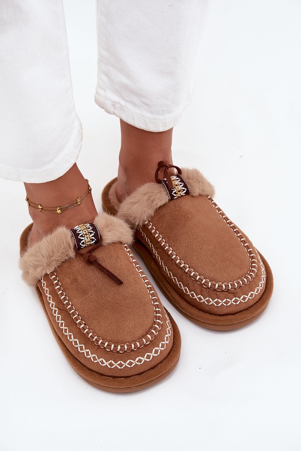 Brown slippers with fur trim worn by a person on a white background